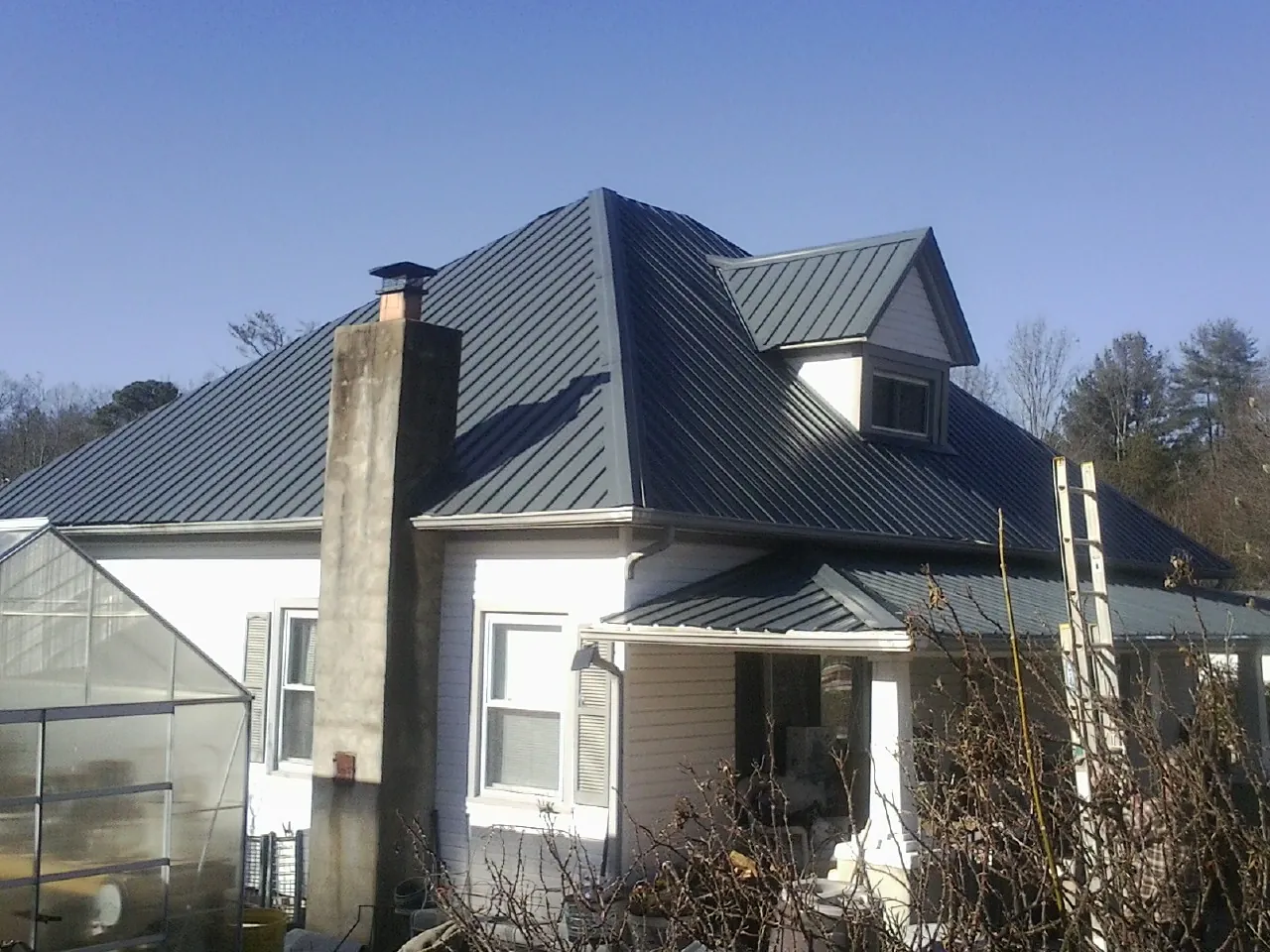 Dark blue standing seam metal roof on a white farmhouse with dormer — Slate & Tile Roof Repair by Roofing Brothers in Gillett