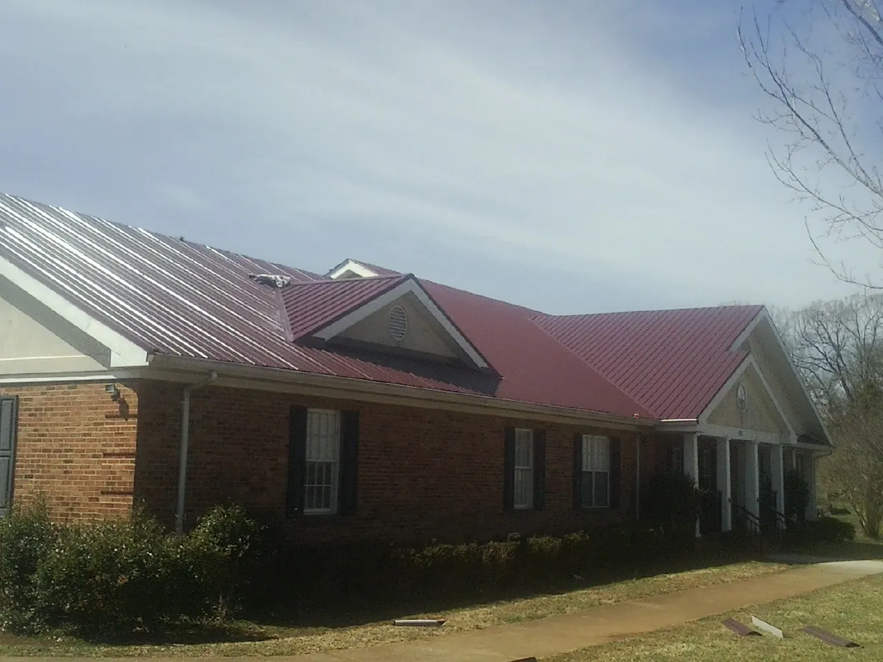 Red metal roof with gabled entries on a long brick building, from a Hail Damage Roof Repair job in Gillett