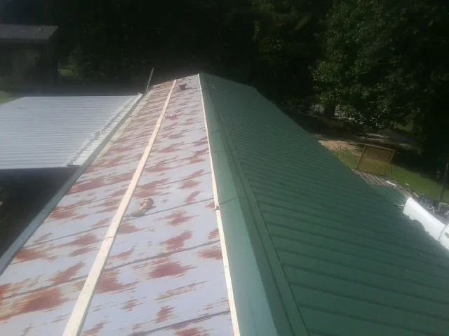 Old rusted panels beside newly installed green metal roofing — Wind Damage Roof Repair by Roofing Brothers in Gillett