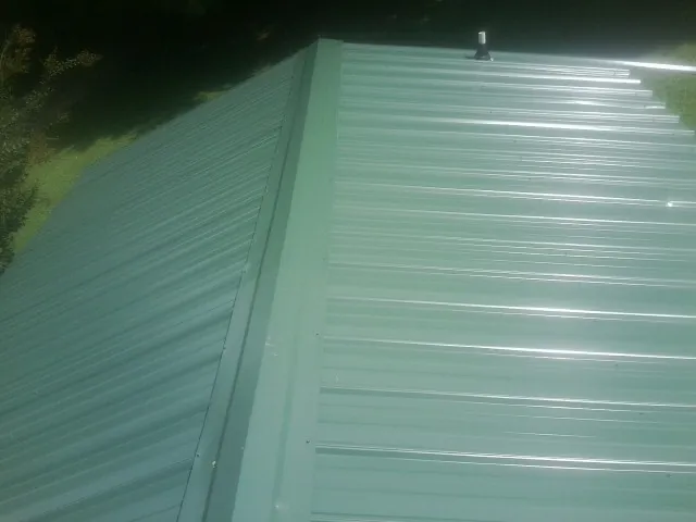New green metal panels meeting at the ridge of a roof — Flat Roof Repair work by our crew in Gillett