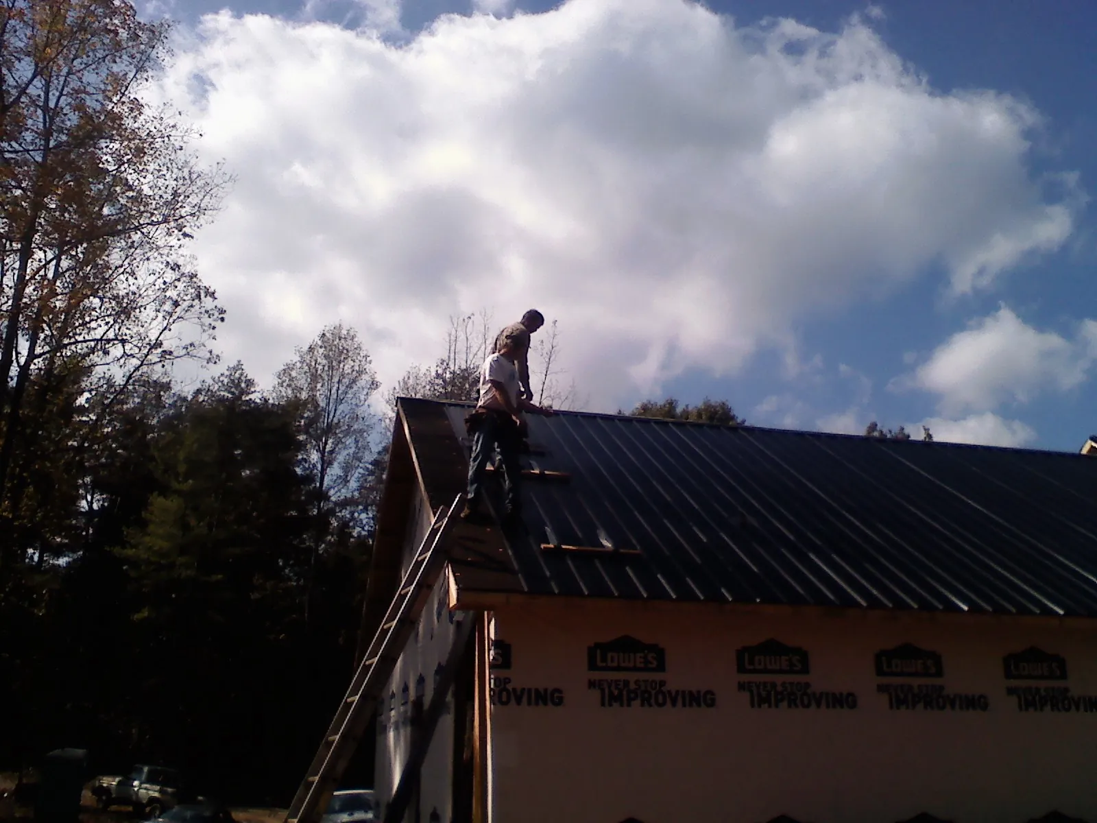 Roofer fastening dark metal panels high against a cloudy sky, from a Roof Inspection job in Gillett