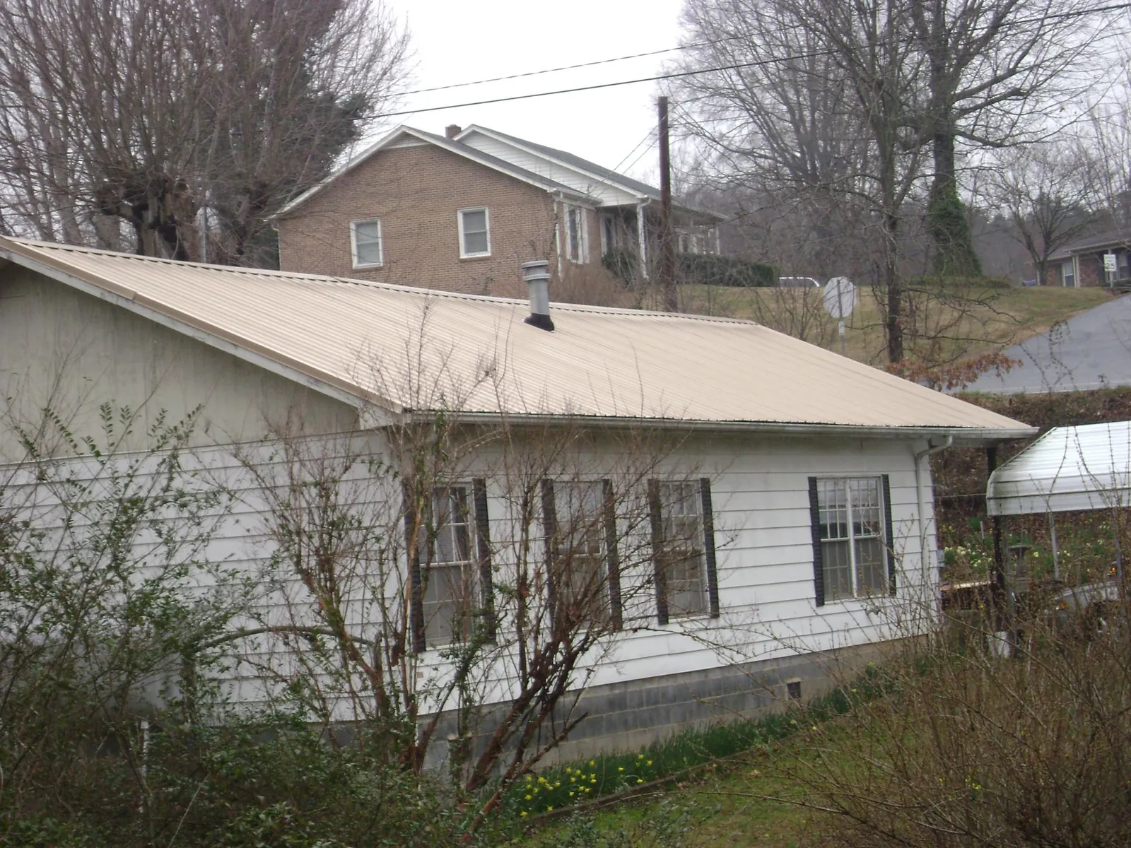 Tan metal roof on a white sided house set into a hillside — Commercial Roofing by Roofing Brothers in Gillett