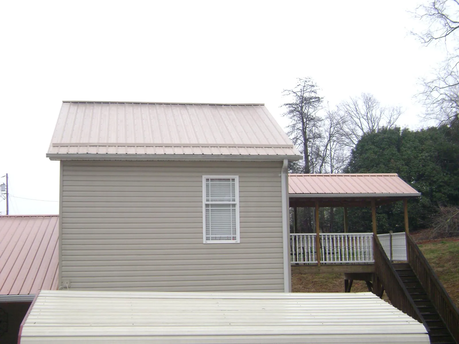 Tan metal roofs on a two story addition and attached porch, from a Roof Replacement job in Gillett